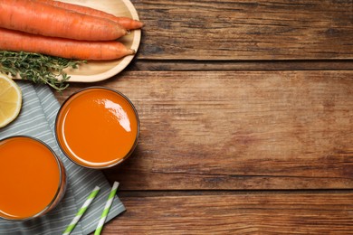 Glasses of tasty juice and fresh carrot on wooden table, flat lay. Space for text