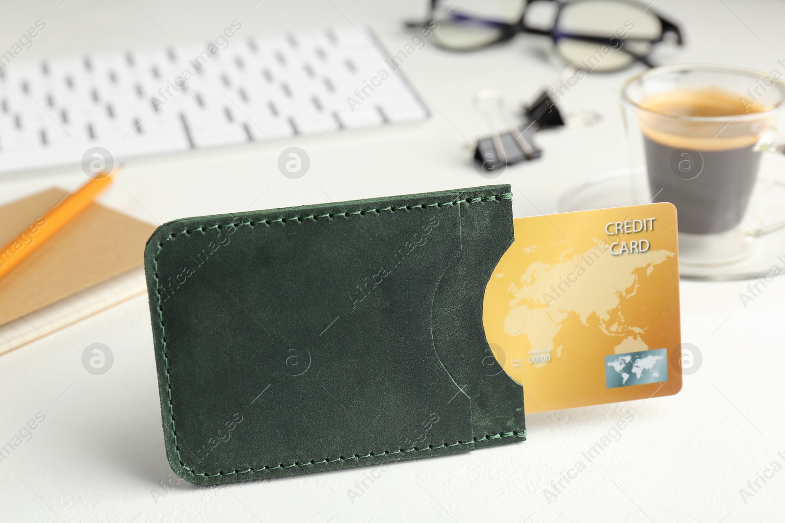 Photo of Leather card holder with credit card, stationery, coffee and keyboard on white table