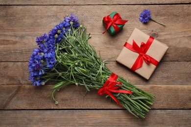 Photo of Bouquet of beautiful cornflowers and gift boxes on wooden table, flat lay