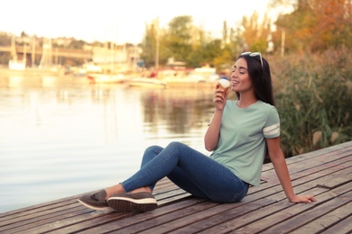 Happy young woman with delicious ice cream in waffle cone outdoors. Space for text