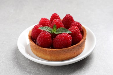 Photo of Tartlet with fresh raspberries and mint on light grey table. Delicious dessert