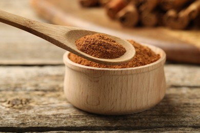 Taking cinnamon powder with spoon from bowl on wooden table, closeup