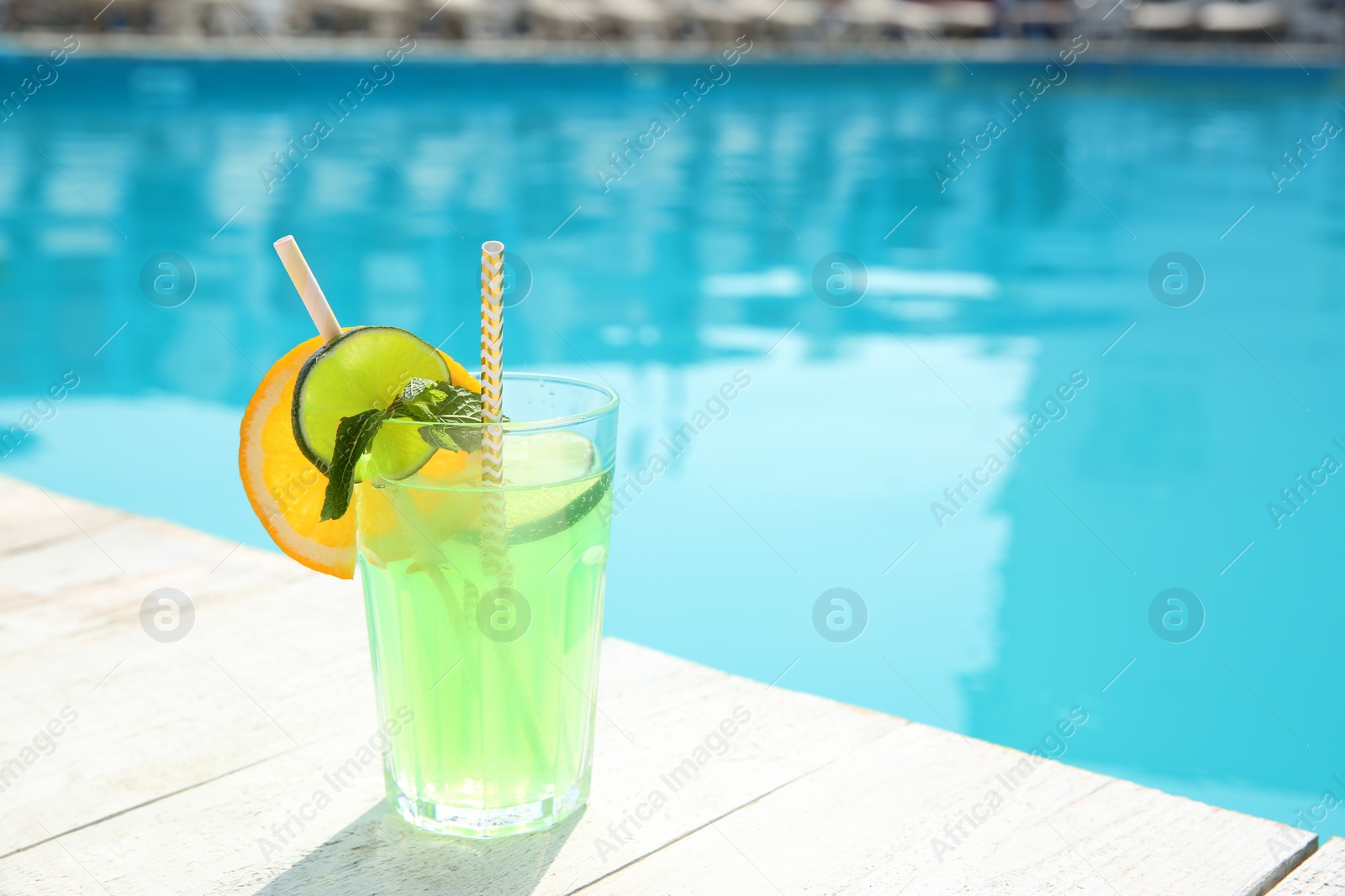 Photo of Refreshing cocktail near outdoor swimming pool on sunny day. Space for text