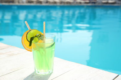 Photo of Refreshing cocktail near outdoor swimming pool on sunny day. Space for text