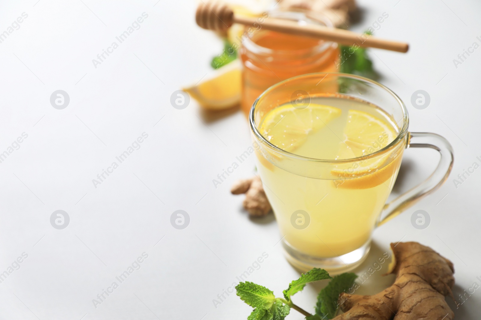 Photo of Glass of aromatic ginger tea and ingredients on light grey background, space for text