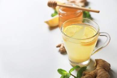 Glass of aromatic ginger tea and ingredients on light grey background, space for text