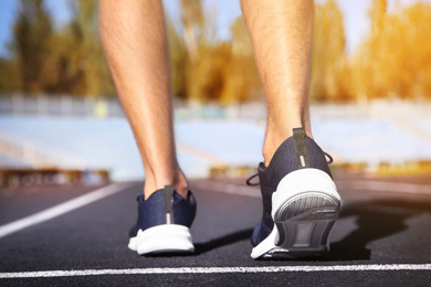 Image of Sporty man running at stadium on sunny morning, closeup