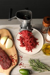 Metal meat grinder with minced beef and spices on light wooden table