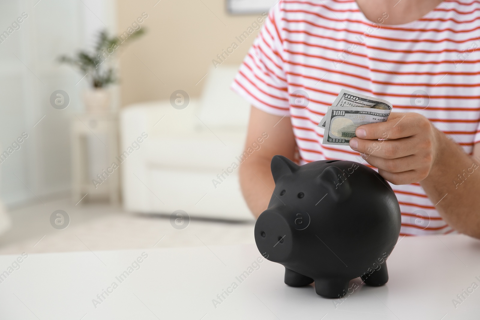 Photo of Man putting money into piggy bank on table indoors. Space for text