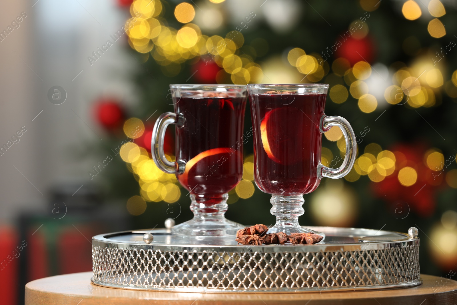 Photo of Hot mulled wine in glass cups and anise stars on table against blurred lights