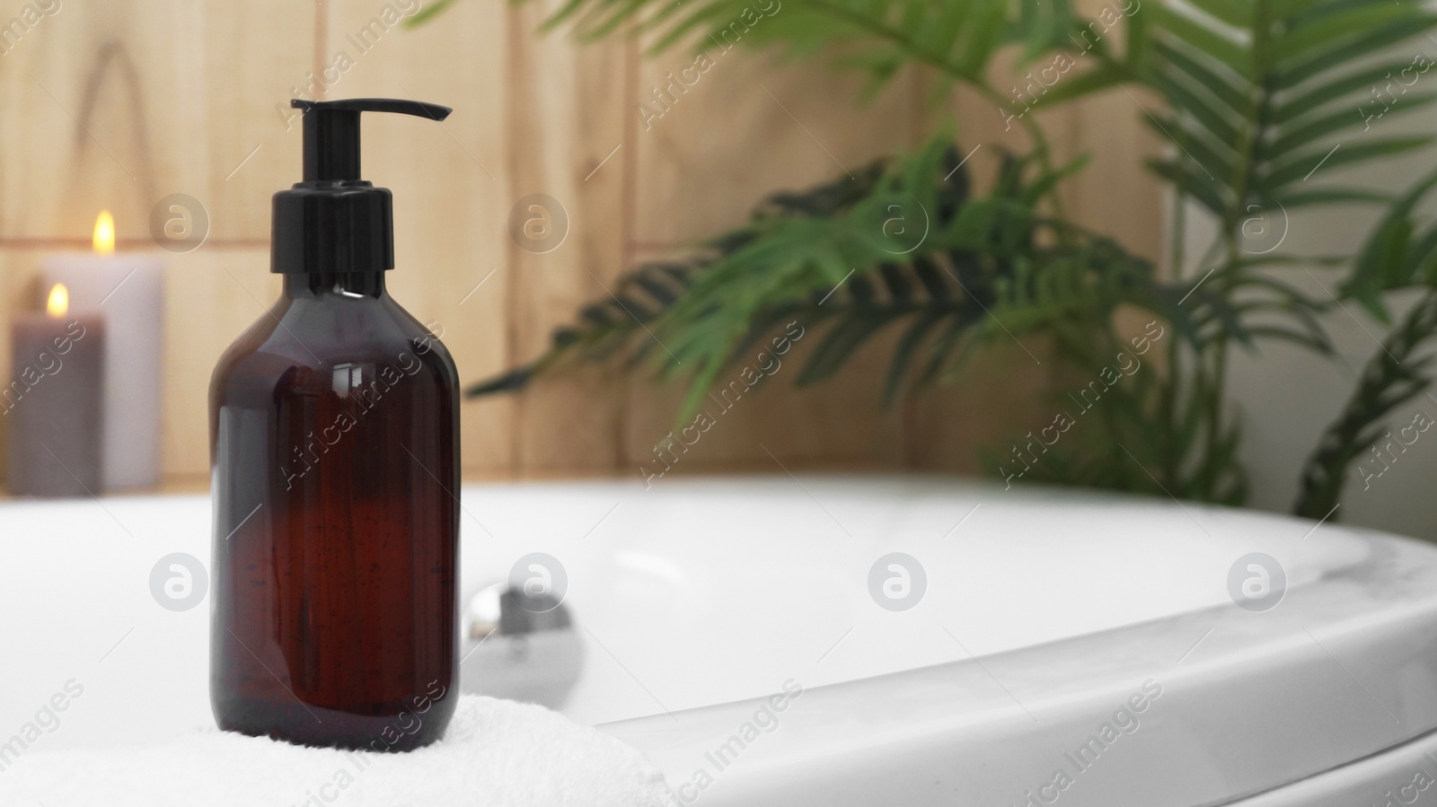 Photo of Black bottle of bubble bath and candles on tub indoors, space for text