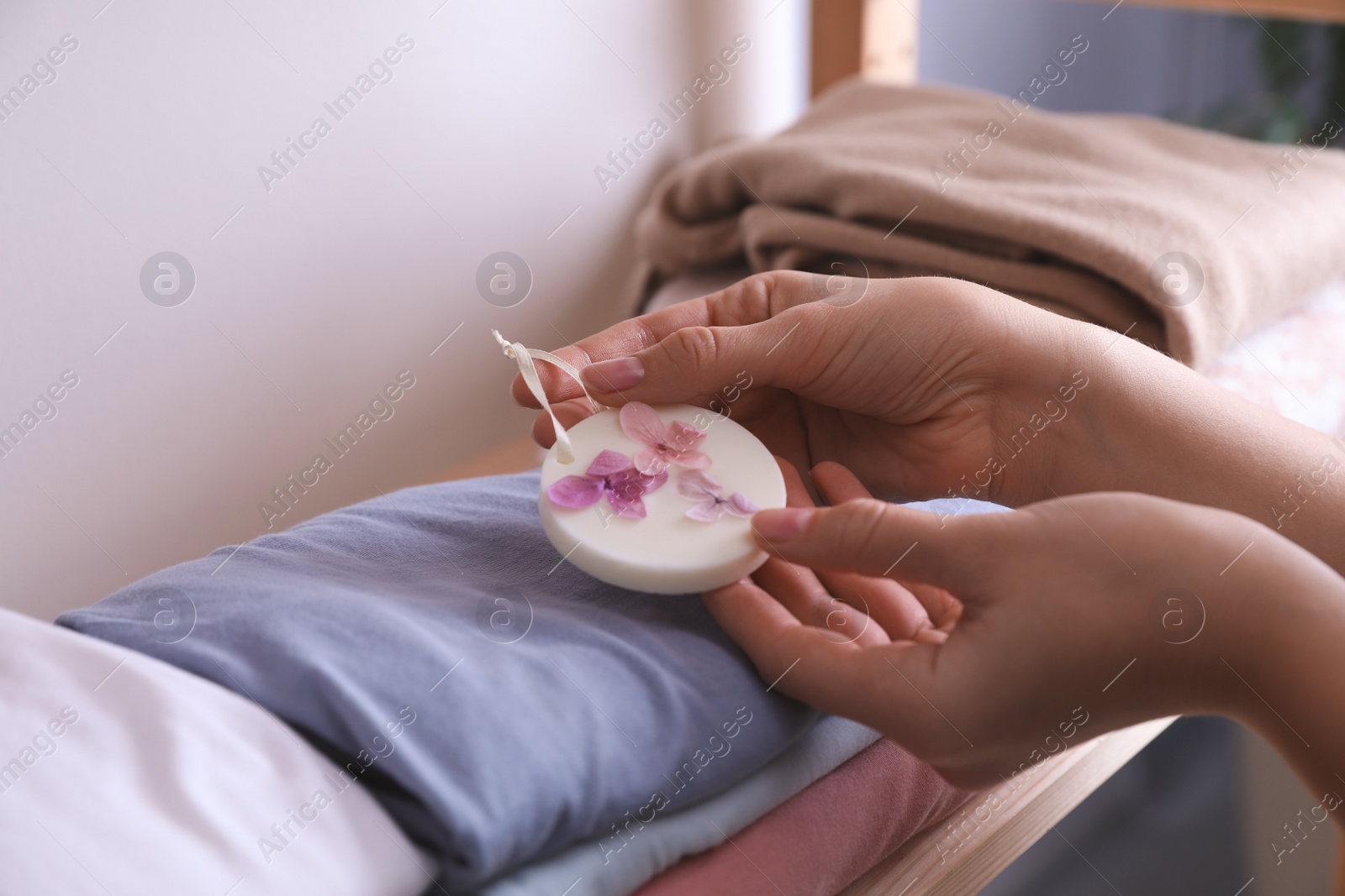 Photo of Woman putting scented wax sachet onto stack of clothes indoors, closeup