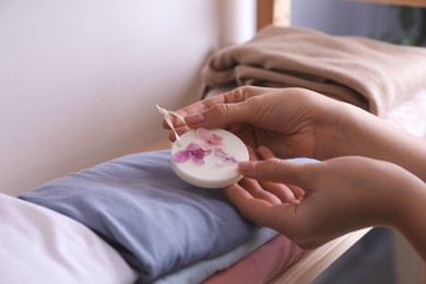 Photo of Woman putting scented wax sachet onto stackclothes indoors, closeup