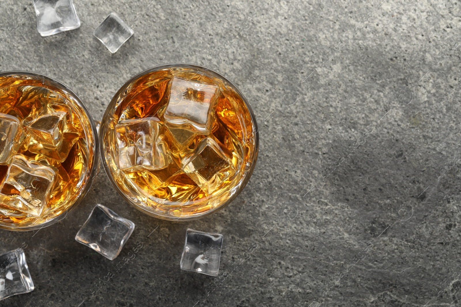 Photo of Whiskey and ice cubes in glasses on grey textured table, top view. Space for text