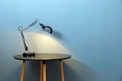 Photo of Modern lamp on table against color background. Space for text