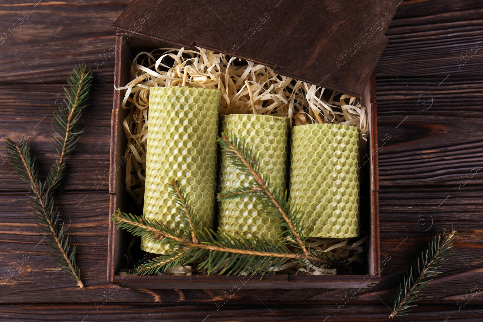 Photo of Stylish elegant beeswax candles with spruce branches on wooden table, flat lay