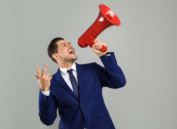 Handsome man with megaphone on grey background