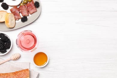 Glass of delicious rose wine and snacks on white wooden table, flat lay. Space for text