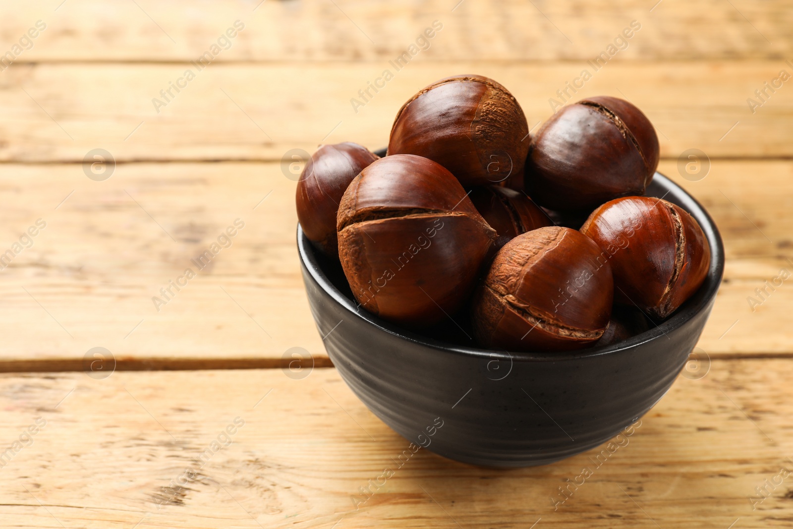 Photo of Fresh edible sweet chestnuts in bowl on wooden table. Space for text