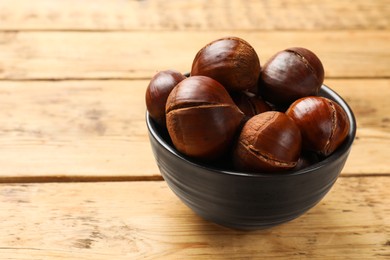 Photo of Fresh edible sweet chestnuts in bowl on wooden table. Space for text