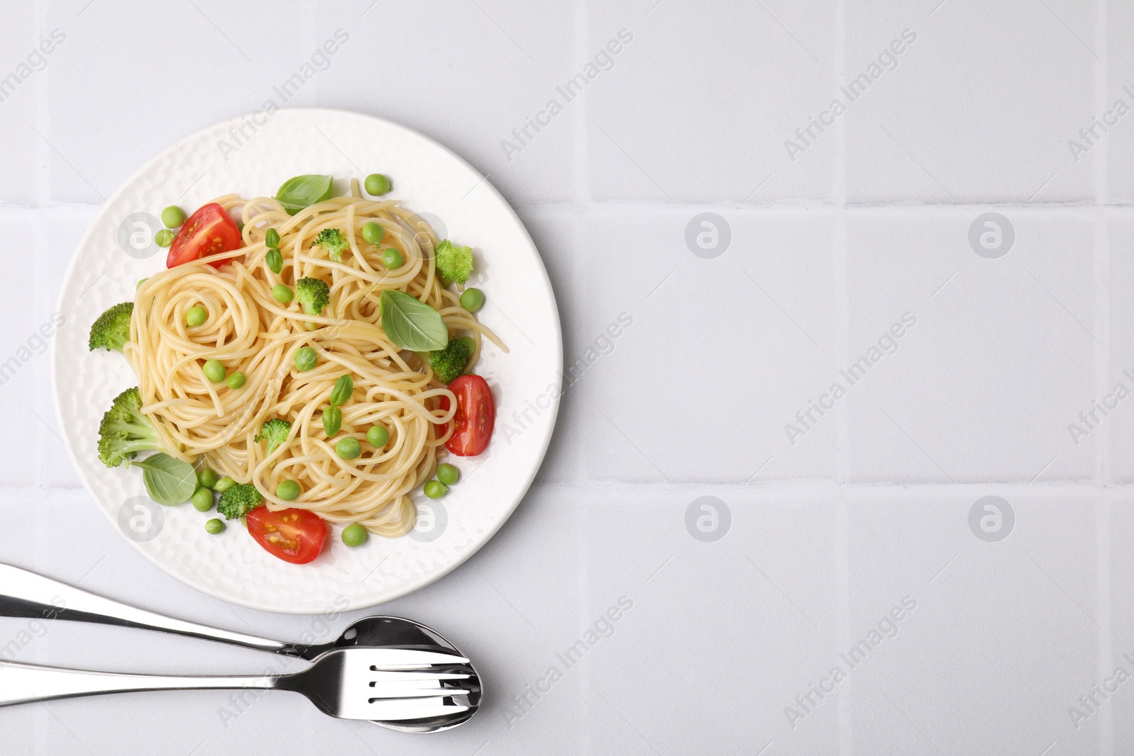 Photo of Plate of delicious pasta primavera and cutlery on white tiled table, flat lay. Space for text