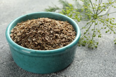 Photo of Bowl of dry seeds and fresh dill on grey table, closeup