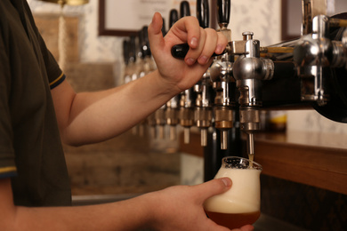 Bartender pouring fresh beer into glass in pub, closeup