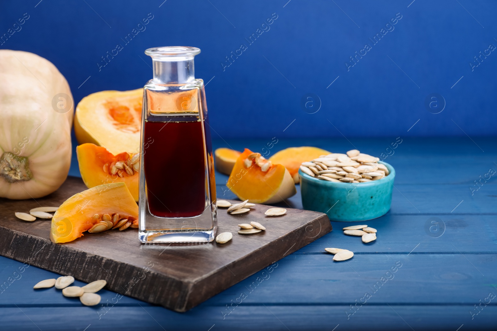 Photo of Fresh pumpkin seed oil in glass bottle on blue wooden table. Space for text