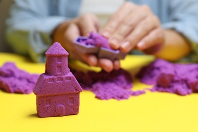 Woman playing with kinetic sand at yellow table, selective focus