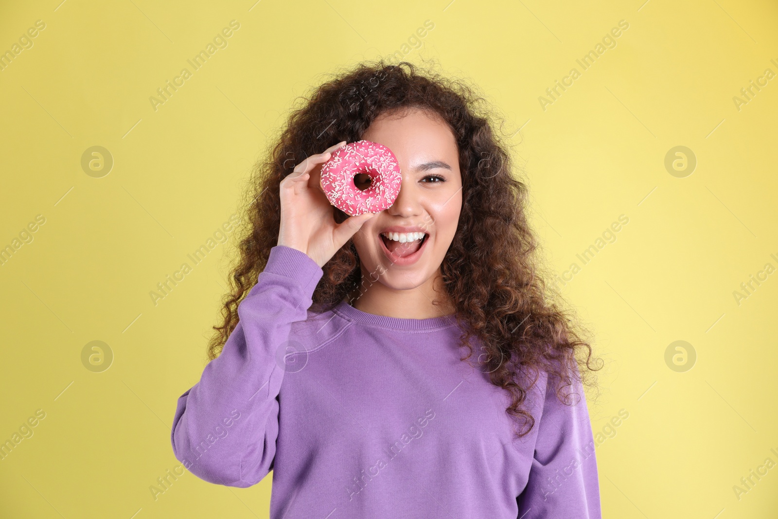 Photo of Beautiful African-American woman with donut on yellow background