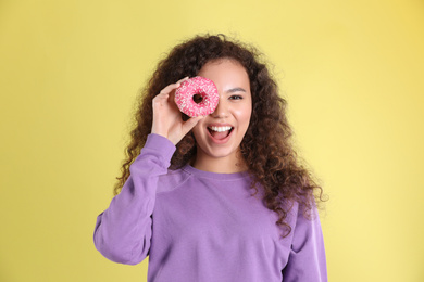 Beautiful African-American woman with donut on yellow background