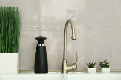 Photo of Modern automatic soap dispenser near sink indoors