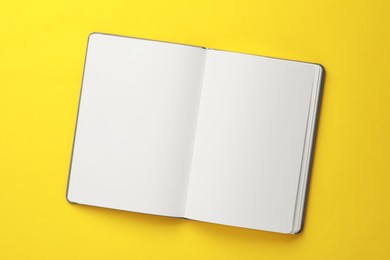 Photo of Open blank notebook on yellow background, top view