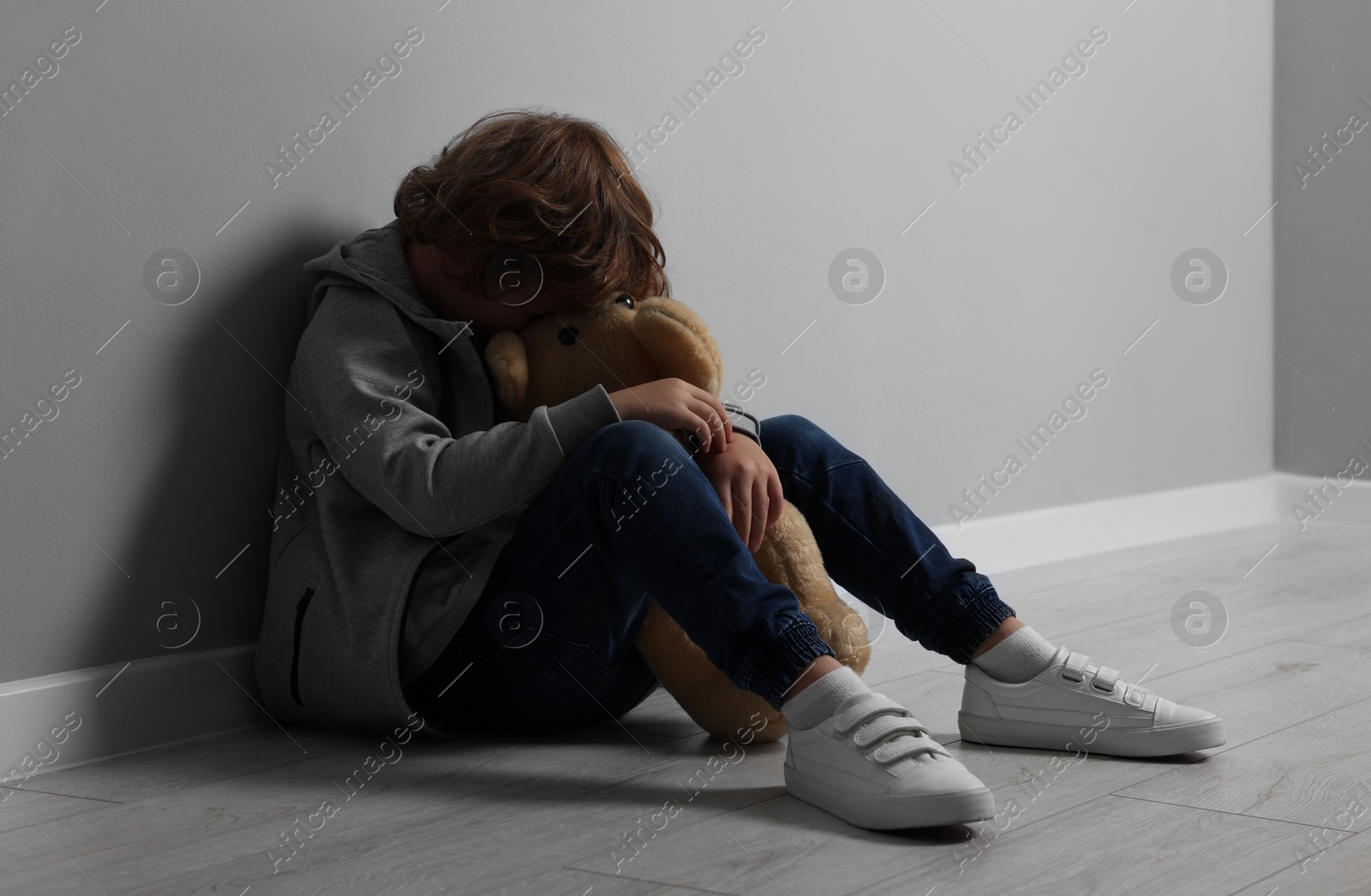 Photo of Child abuse. Upset boy with toy sitting on floor near grey wall