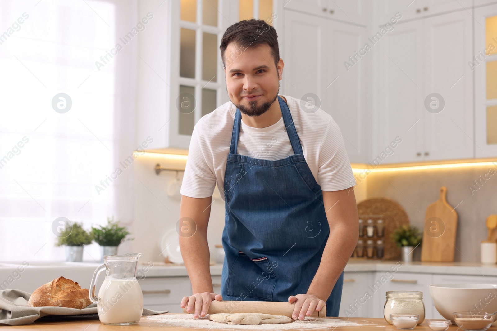 Photo of Making bread. Man rolling dough at wooden table in kitchen