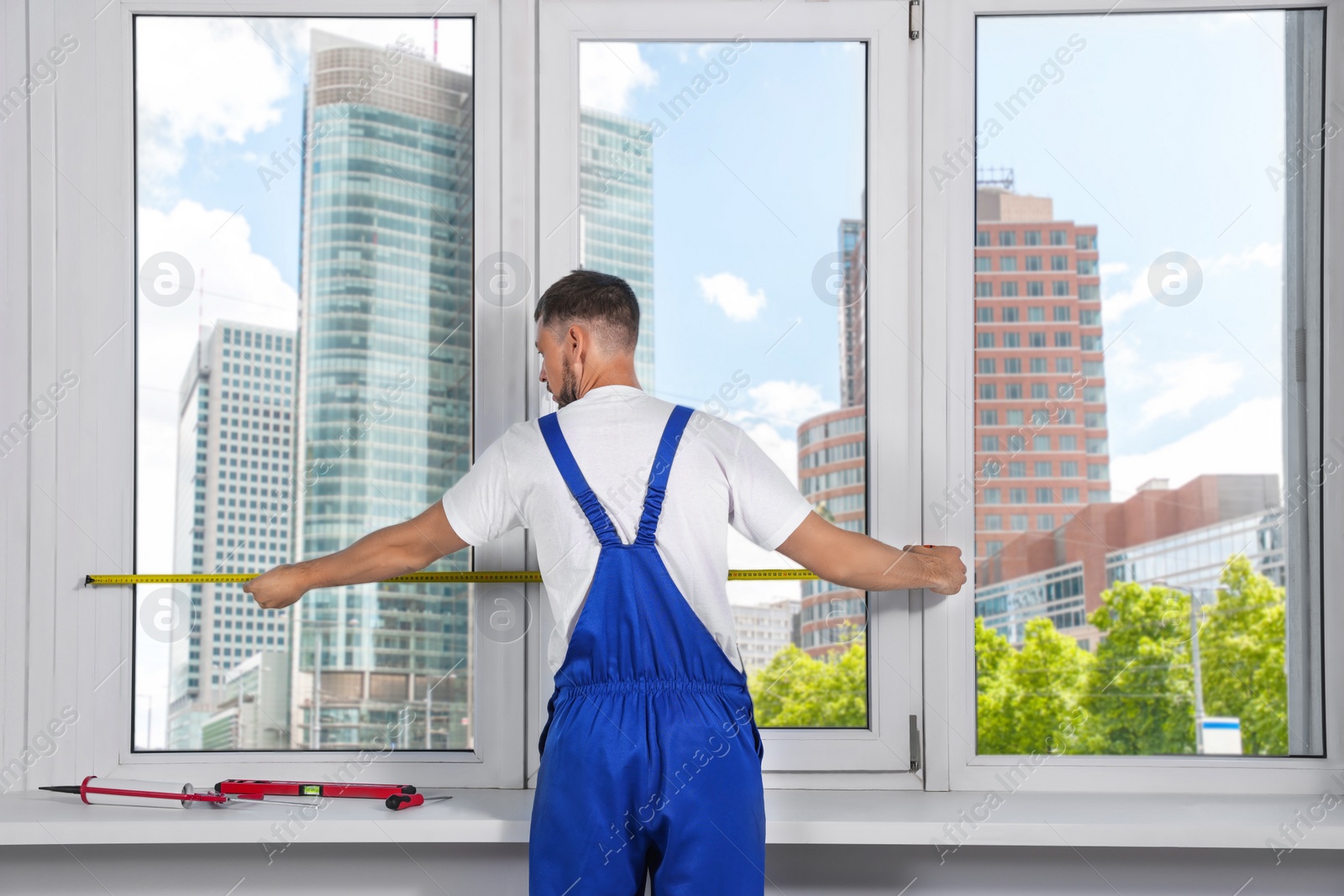 Photo of Worker measuring plastic window indoors, back view. Installation process