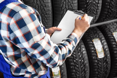 Male mechanic with clipboard near tires in automobile service center, closeup