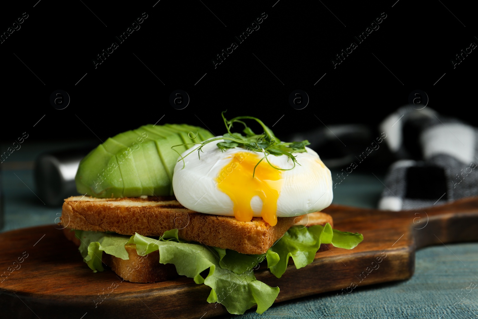 Photo of Delicious poached egg with toasted bread and avocado served on wooden board, closeup