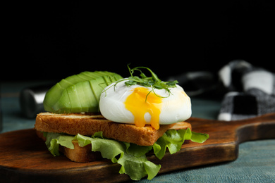 Delicious poached egg with toasted bread and avocado served on wooden board, closeup