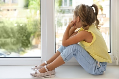 Photo of Cute little girl on window sill at home