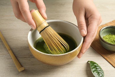 Woman preparing matcha tea at wooden table, closeup