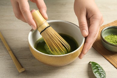 Photo of Woman preparing matcha tea at wooden table, closeup