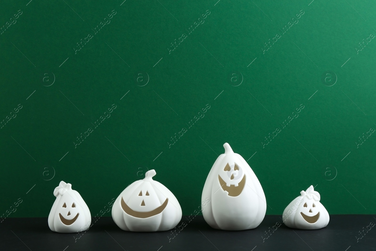 Photo of White pumpkin shaped candle holders on black table against green background, space for text. Halloween decoration