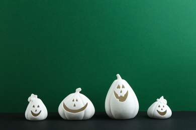 White pumpkin shaped candle holders on black table against green background, space for text. Halloween decoration