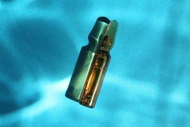 Skincare ampoule in sunlight on light blue background, top view