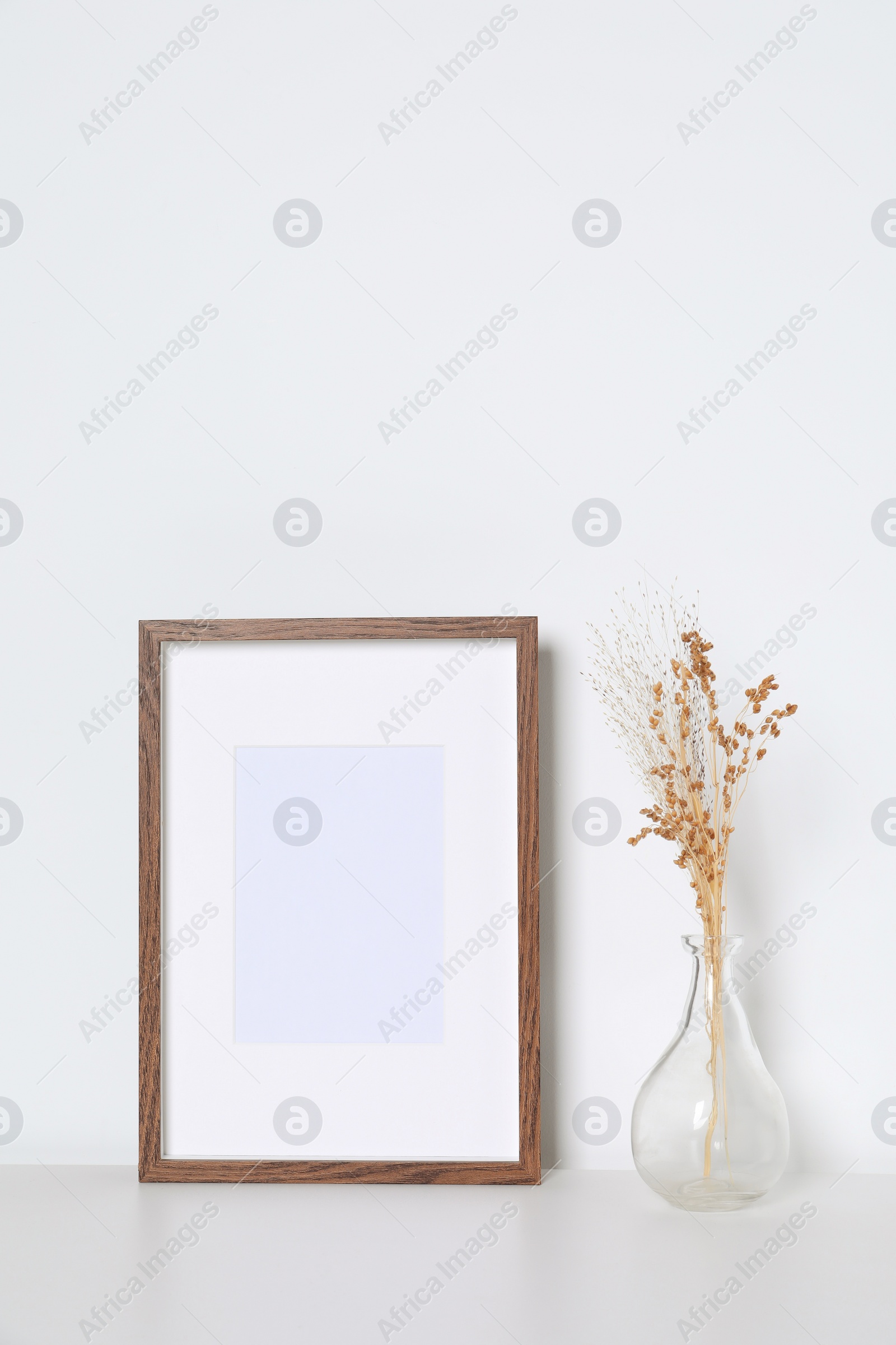 Photo of Empty photo frame and vase with dry decorative flowers on white table. Mockup for design