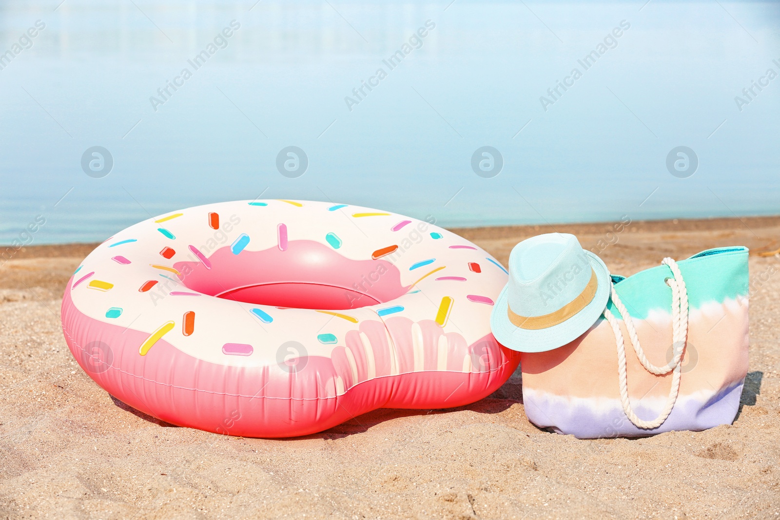 Photo of Colorful inflatable ring, hat and bag on sand. Beach object