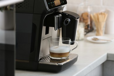 Modern espresso machine and glass cup of coffee on white marble countertop in kitchen