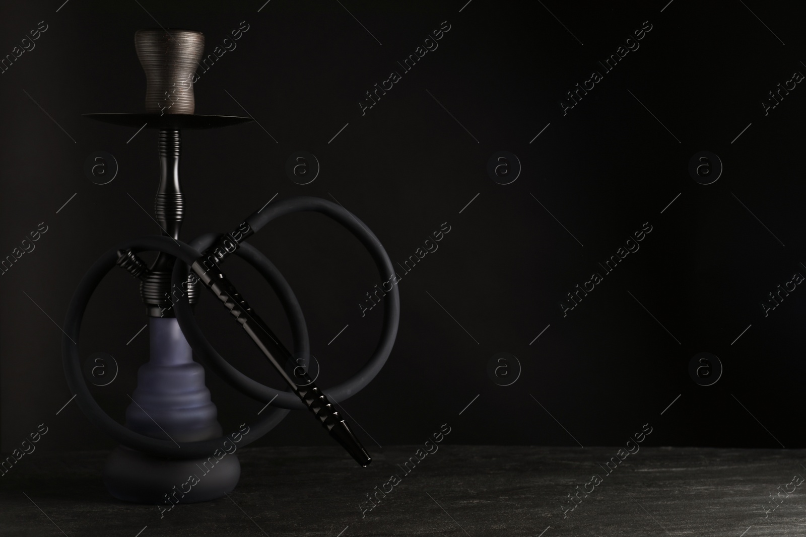 Photo of Modern hookah on black table against dark background, space for text