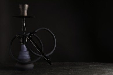 Photo of Modern hookah on black table against dark background, space for text